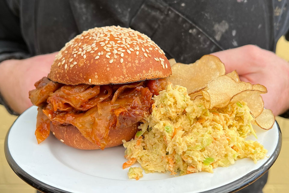 a burger being served on plate with a side of chips and coleslaw