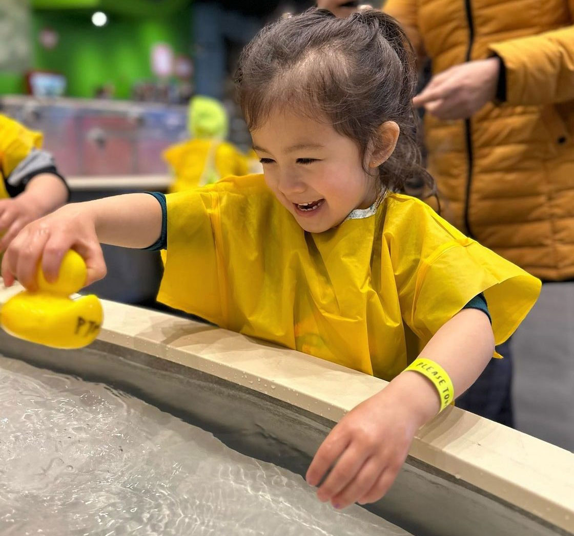 little girl with yellow coat playing with a rubber duck